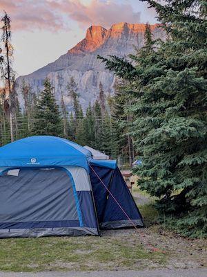 Blue tent on a campsite, with a gorgeous mountain beautifully lit by the sunrise in the background